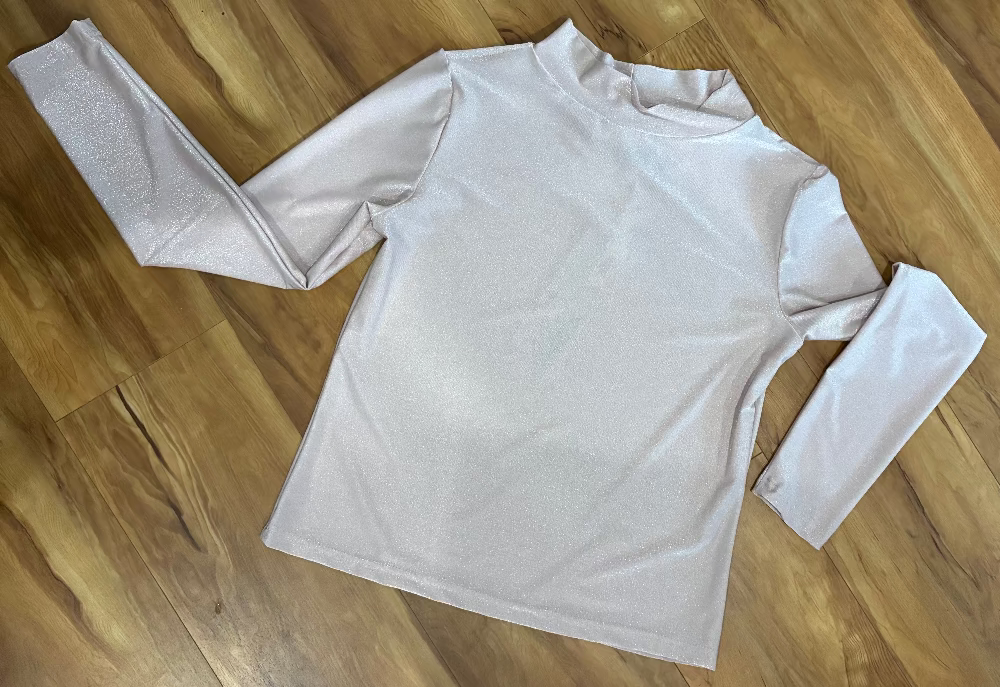 Pale pink long-sleeve shirt with slight mock neck on a wooden floor